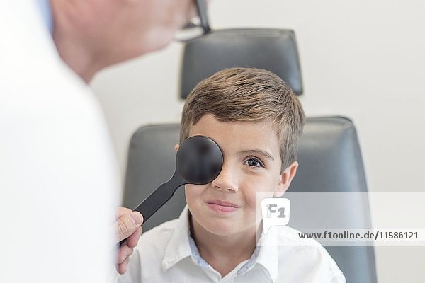 Männlicher Optiker testet die Sehkraft eines Jungen.