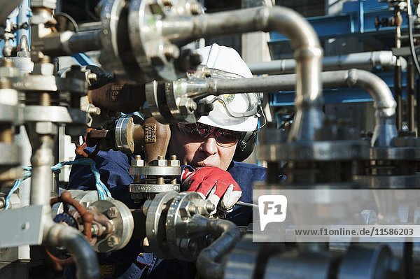 MODELL FREIGEGEBEN. Arbeiter  der eine Pumpe in einer Öl- und Gasraffinerie überprüft.