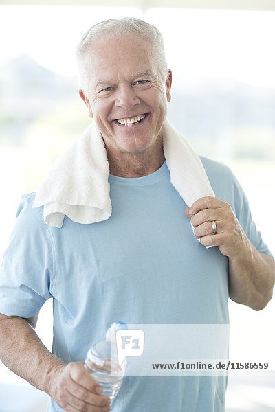 Älterer Mann im Fitnessstudio mit Wasserflasche und Handtuch.