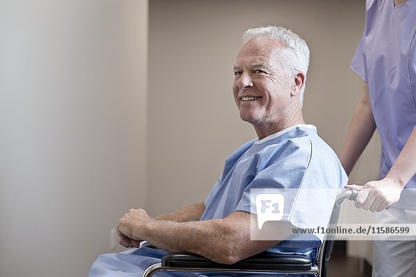 Senior man in hospital gown in wheelchair  smiling.