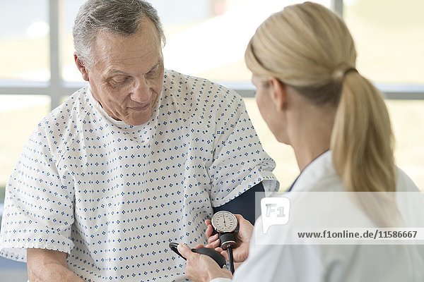 Female doctor taking senior man's blood pressure.