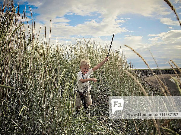 Junge spielt mit Schwert im Weizenfeld