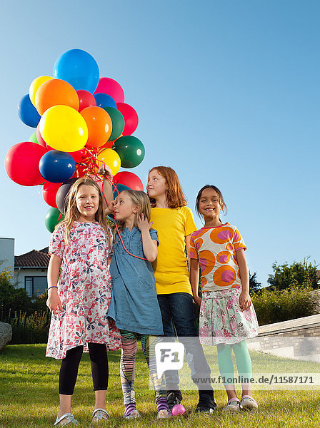 Girls standing on lawn holding multicoloured balloons