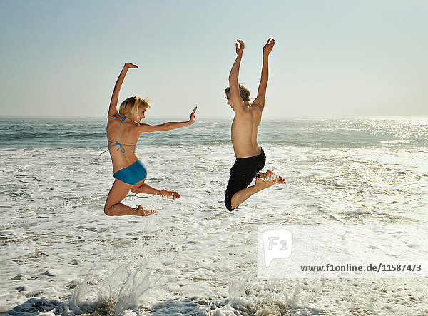 Paar springt am Strand in Wellen