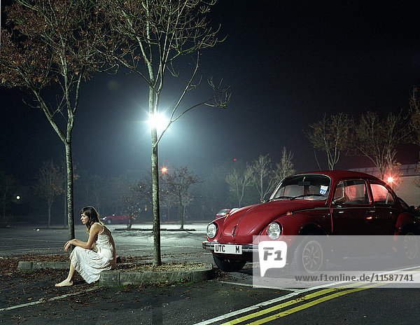 Frau  die nachts auf einem Parkplatz sitzt