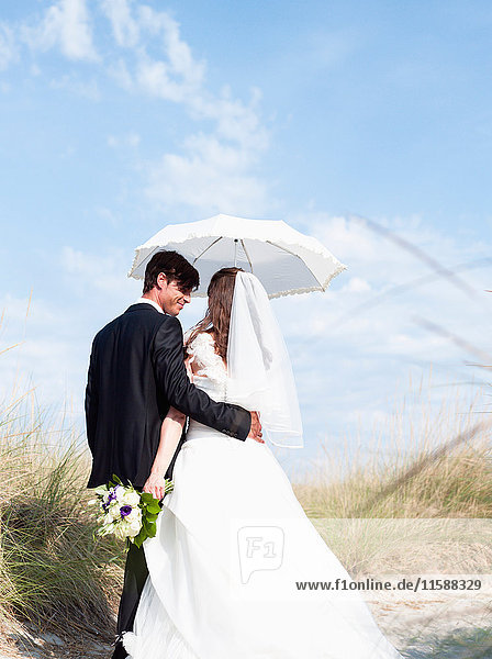Braut und Bräutigam gehen unter dem Sonnenschirm