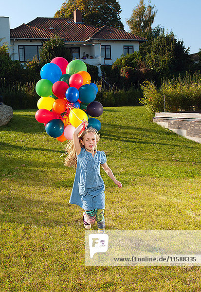 Girl running across lawn with multicoloured balloons