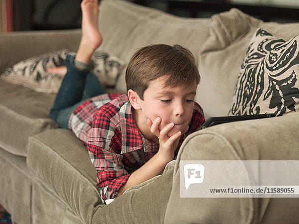 Junge spielt mit digitalem Tablett auf Sofa