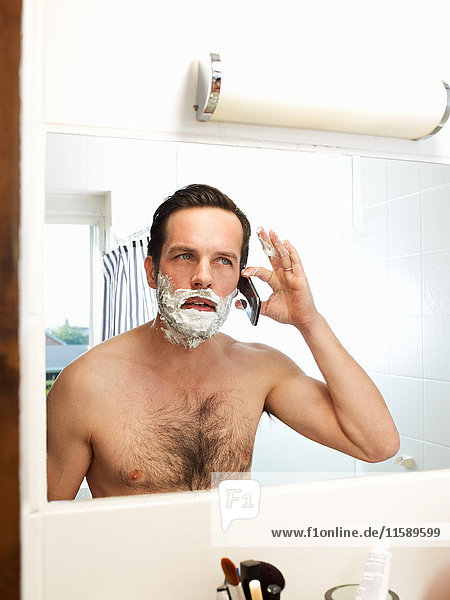 Mature man in shaving foam listening to cellphone
