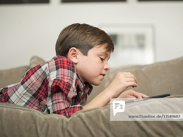 Junge spielt mit digitalem Tablett auf Sofa  Seitenansicht