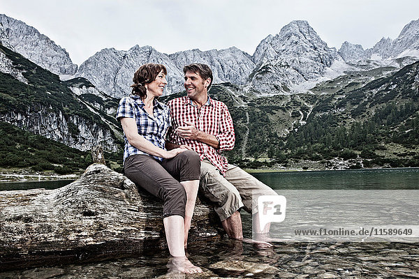 Lächelndes Paar mit baumelnden Füßen im See