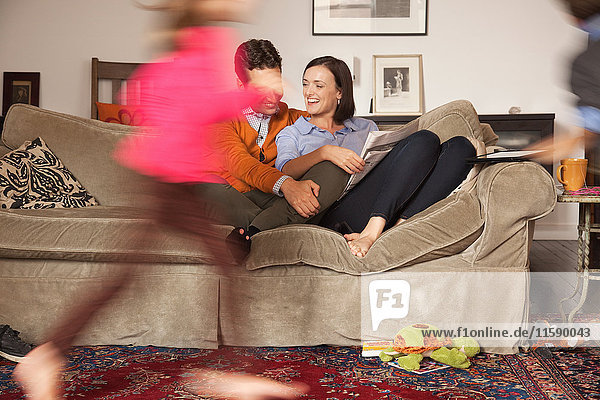Mittleres erwachsenes Paar auf dem Sofa mit Kindern  die sich um sie herum bewegen.