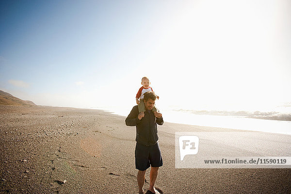 Vater trägt Sohn auf den Schultern am Strand entlang