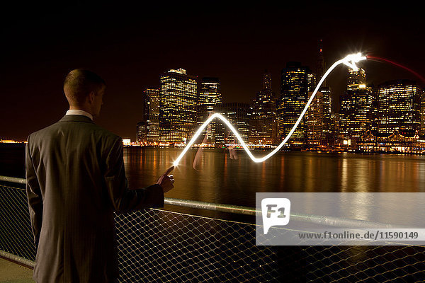 Geschäftsmann  der nachts eine Lichtspur am East River zieht  Brooklyn  USA