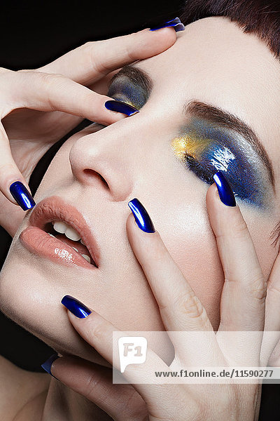 Junge Frau mit blauem Nagellack und Lidschatten im Gesicht