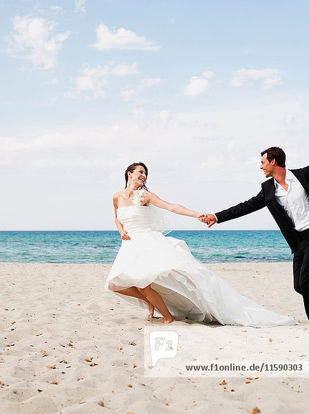bride and groom running along beach