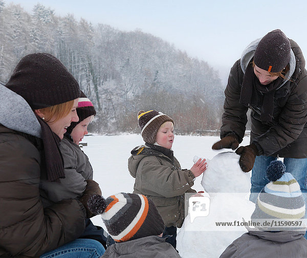 Frauen und Kinder bauen Schneemann