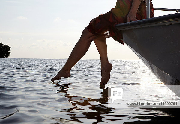 Ältere Frau sitzt auf der Kante eines Motorbootes mit den Füßen im Wasser