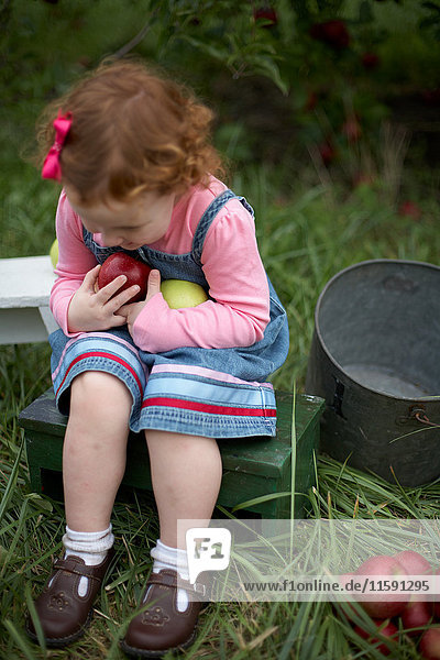 Mädchen sitzt auf Bank und hält Äpfel