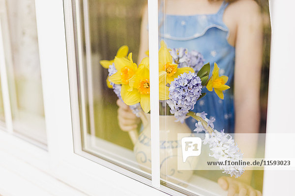 Blumenvase aus Narzissen und Hyazinthen hinter der Fensterscheibe