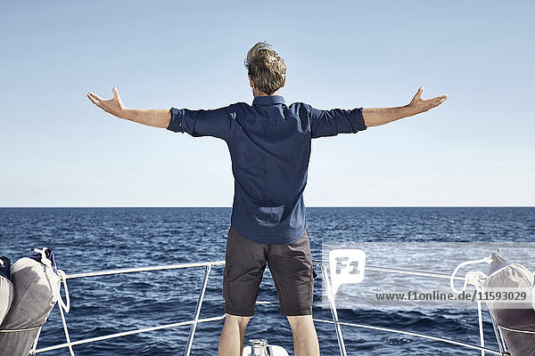 Back view of mature man standing on his motor yacht with arms outstretched