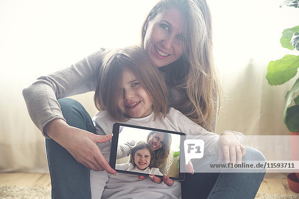 Porträt von Mutter und kleiner Tochter zu Hause mit Tablette und Selfie