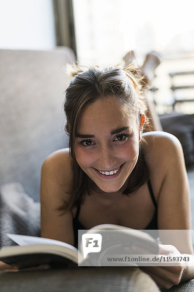 Lächelnde junge Frau in Dessous Lesebuch auf Couch
