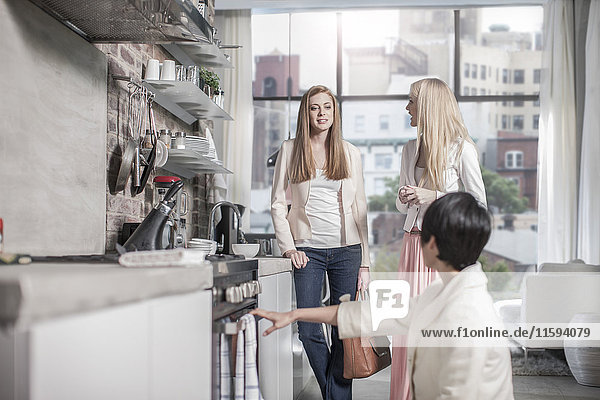 Three female friends in modern kitchen with city view