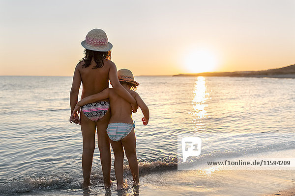 Spanien  Menorca  zwei Mädchen beobachten den Sonnenuntergang am Strand