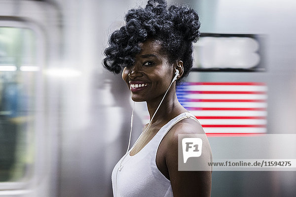 USA  New York City  Manhattan  Portrait einer glücklichen Frau mit Kopfhörern auf dem Bahnsteig der U-Bahnstation