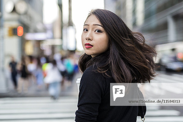 USA  New York City  Manhattan  Porträt einer jungen Frau  die beim Überqueren der Straße über die Schulter schaut.