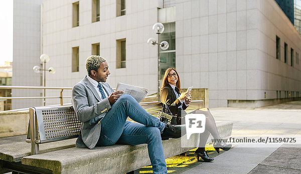 Ein junger Geschäftsmann und eine junge Frau  die auf einer Bank sitzen und reden.