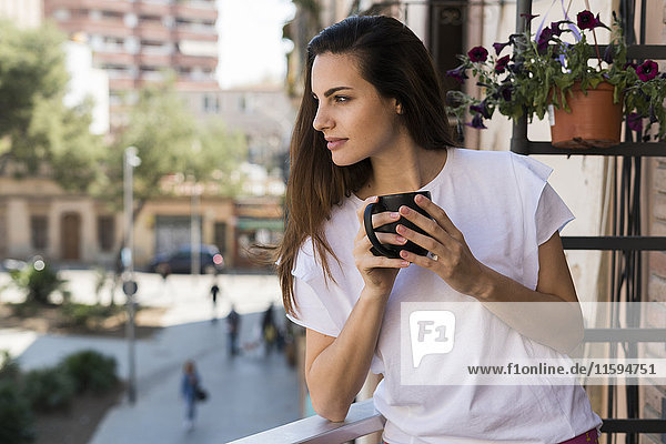 Woman with coffee mug standing on balcony looking at distance