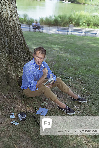 Mann sitzt auf einer Wiese im Park mit Notizbuch