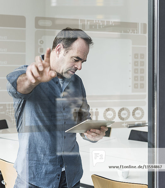Businessman with tablet touching glass pane with data in office