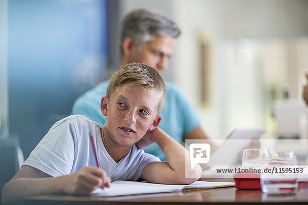 Boy doing homework with father in background