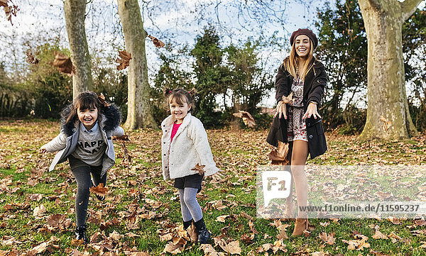 Mother throwing leaves with her daughters in autumnal park