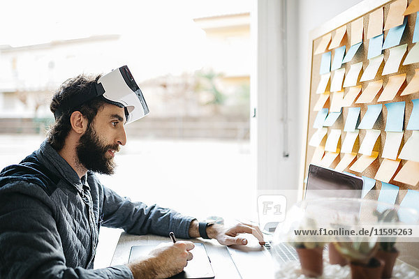 Mann mit Virtual Reality Brille bei der Arbeit mit Grafiktablett und Laptop im Büro