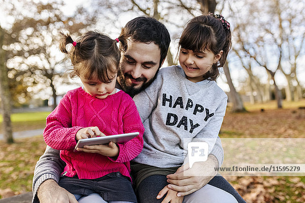 Father with his little daughters looking at tablet in autumnal park