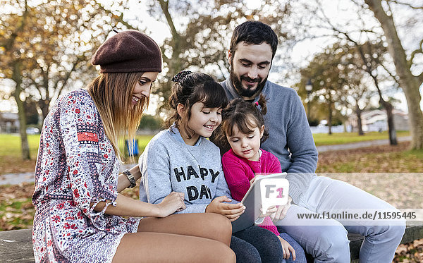 Family sitting on bench in autumnal park looking at tablet