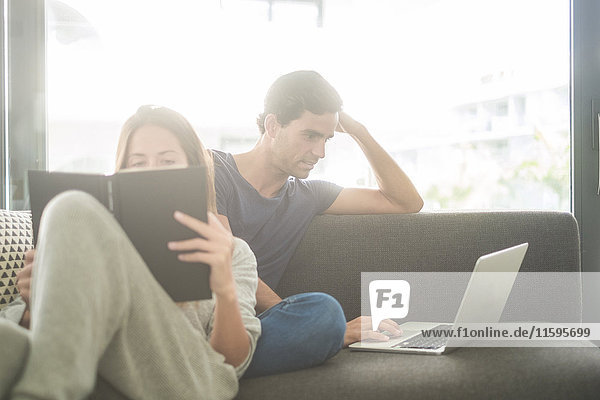 Young couple on couch with book and laptop