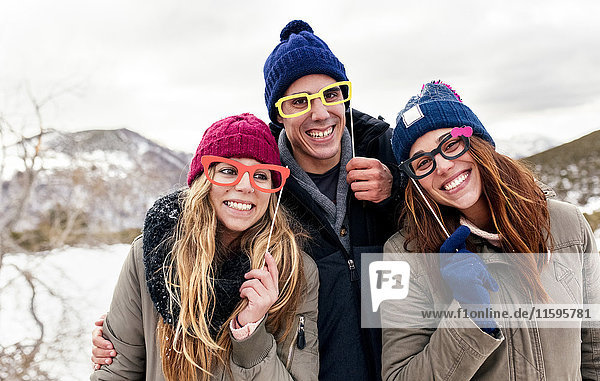 Three friends with fake glasses having fun in the snowy mountains