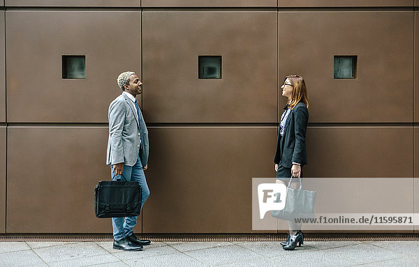 Young businessman and woman standing in front of steel wall  talking
