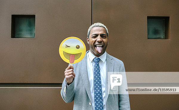 Geschäftsmann hält Emoji lächelnd mit herausstehender Zunge in der Hand