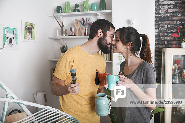Young couple kissing between paintbrushes and tea mugs