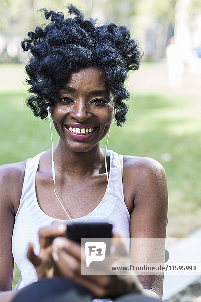 Portrait od smiling woman using cell phone and earphones in a park