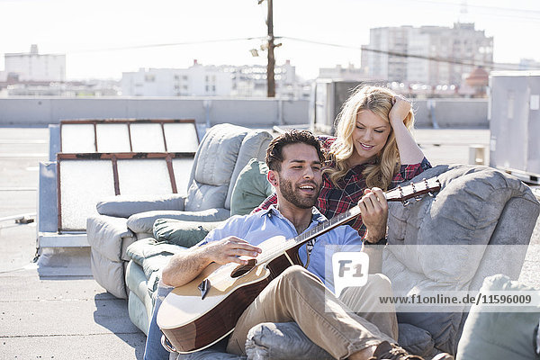 Couple on rooptop sitting on sofa and playing guitar