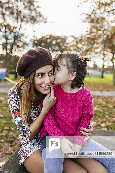 Kleines Mädchen  das seine Mutter im Herbstpark küsst.