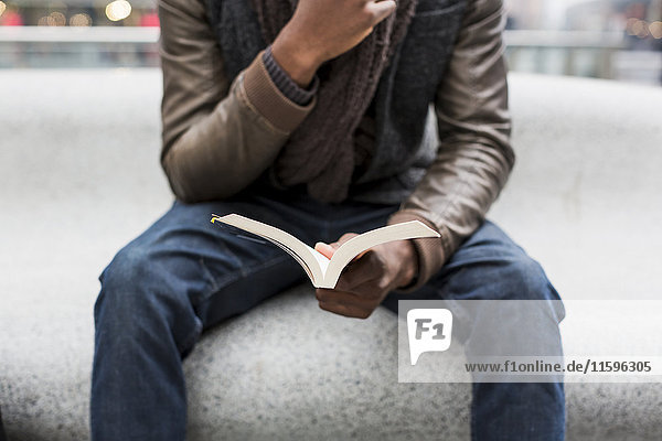 Young man sitting on bench reading a book  partial view