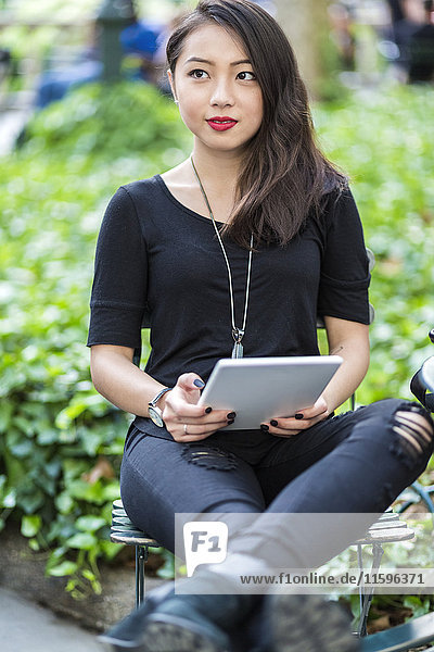 Portrait of young woman with tablet sitting at city park